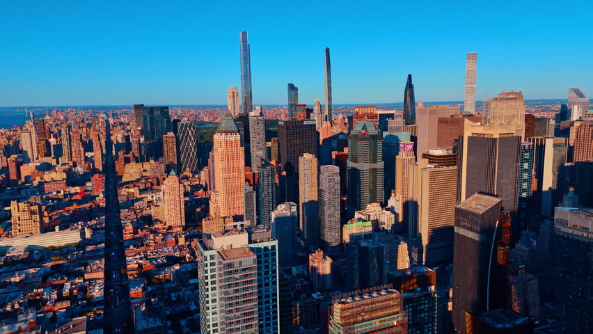Tall skyscrapers of Manhattan skyline under clear blue sky. Aerial view looking over the city toward distant landmarks and high rise developments.