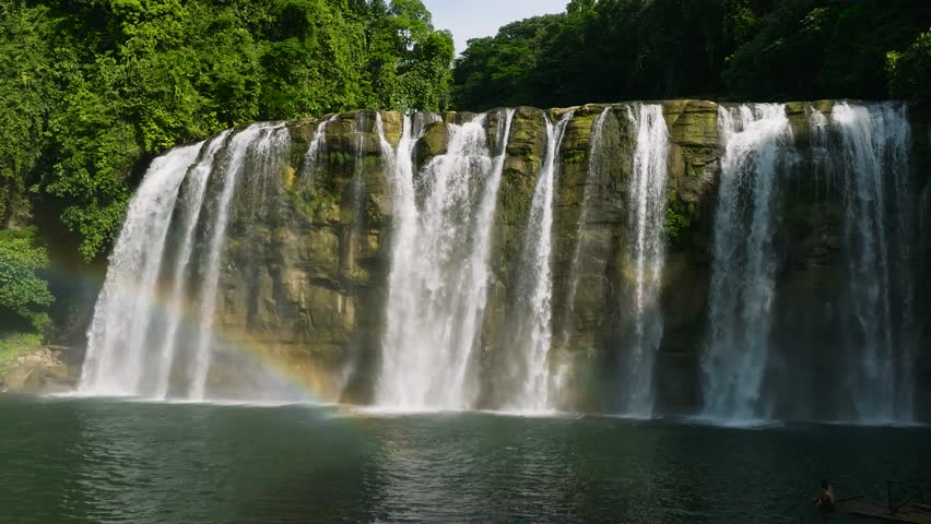 Falls with white curtain-like and mist with sunlight reflection and rainbow. Bislig, Surigao del Sur. Philippines. Slow motion.