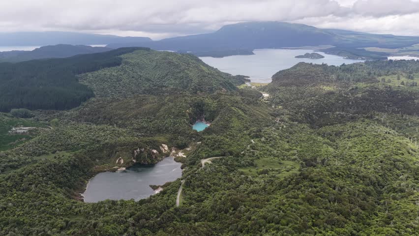 Aerial view over lush green hills and lakes under cloudy sky in remote natural landscape.