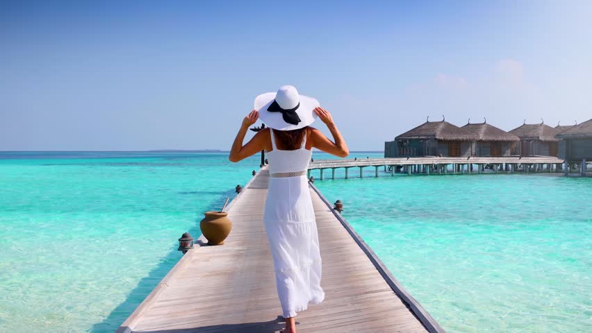 A happy luxury woman in white summer dress walks over a wooden pier in the Maldives islands and enjoys her tropical holidays