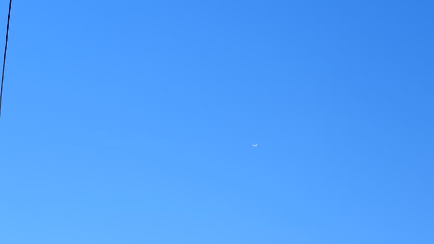 A small bright moon visible in a clear blue daytime sky. Minimalist natural scene with soft light and tranquil atmosphere.