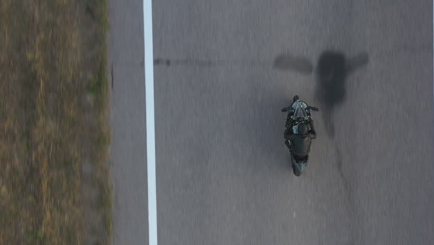 Top view to biker riding on modern sport motorbike at highway. Motorcyclist racing his motorcycle on asphalt road. Man in helmet drive bike during trip. Concept of freedom and adventure. Aerial shot