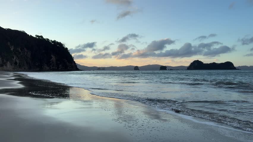 Waves washing over wet sand creating reflections at Hahei Beach, New Zealand.