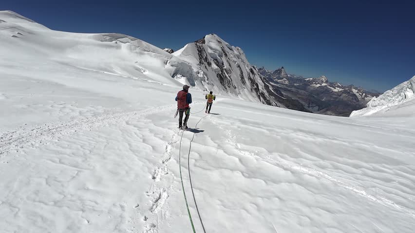 POV mountaineering in rope team with mountaineers descending on glacier Grenzgletscher and mountain panorama with summits Lyskamm and Matterhorn in Pennine Alps, Switzerland