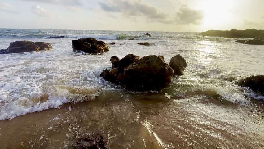 Powerful ocean waves crashing over coastal rocks at sunset in South Goa