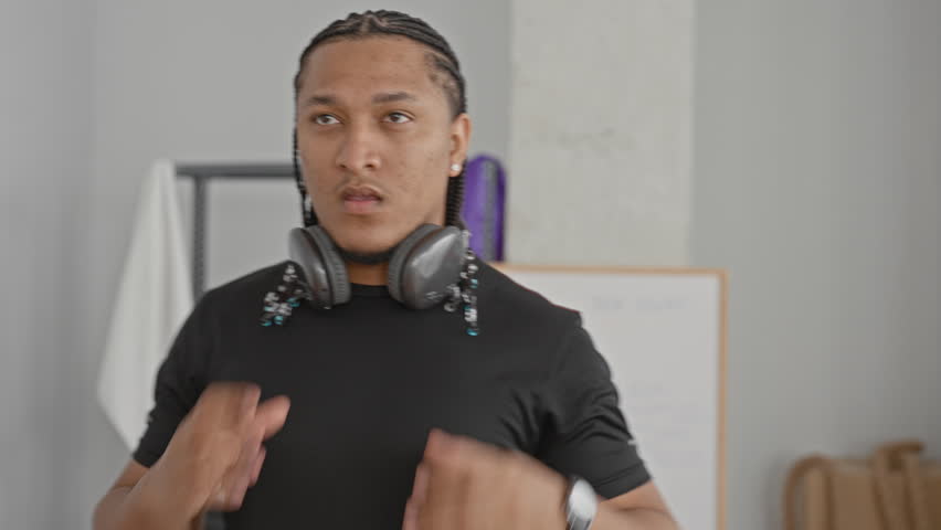 Man adjusting headphones and listening while training with braided hair and beads in a workout studio; determination.