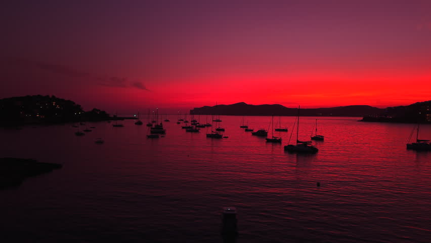Sailboats resting on calm water during a vibrant, red sunset in mallorca, spain