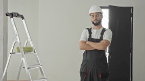 Man in hardhat and overalls gives thumbs up beside ladder and paint roller inside building; confidence accomplishment. - Powered by Shutterstock - Get 15% off with code: PIKWIZARD15
