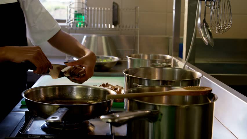 Female chef slicing mushrooms and moving them into pan, cooking as UI icons floating toward hands. Kitchen, professional, prep, stove, overlay, motion, stainless