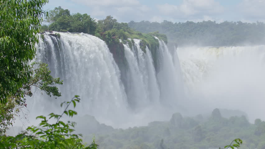 Powerful Iguazu waterfall with strong water flow surrounded by green trees