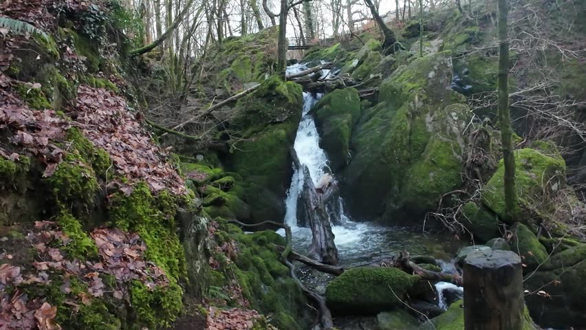 Serene Winter River Flowing Over Rocks. Peaceful Mosscovered Waterfall Amidst Autumn Leaves And Mist