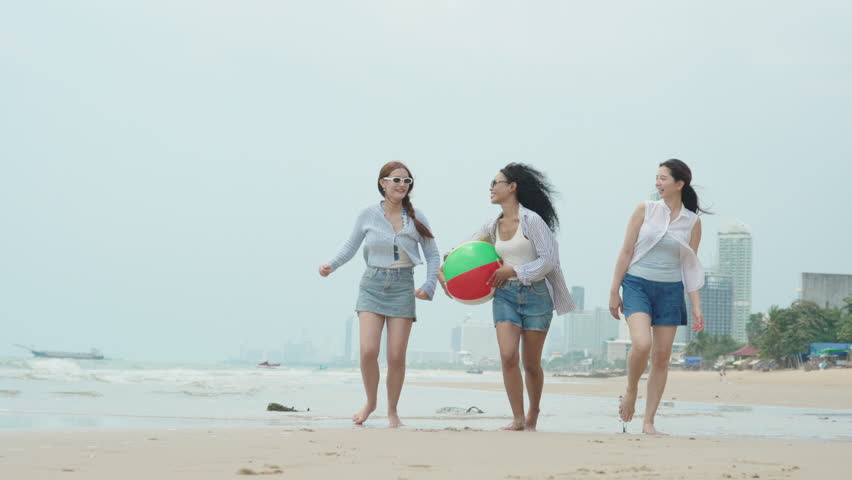 Joyful slow-motion video of three young diverse female friends running and simultaneously jumping together on a tropical sandy beach during a sunny summer vacation.