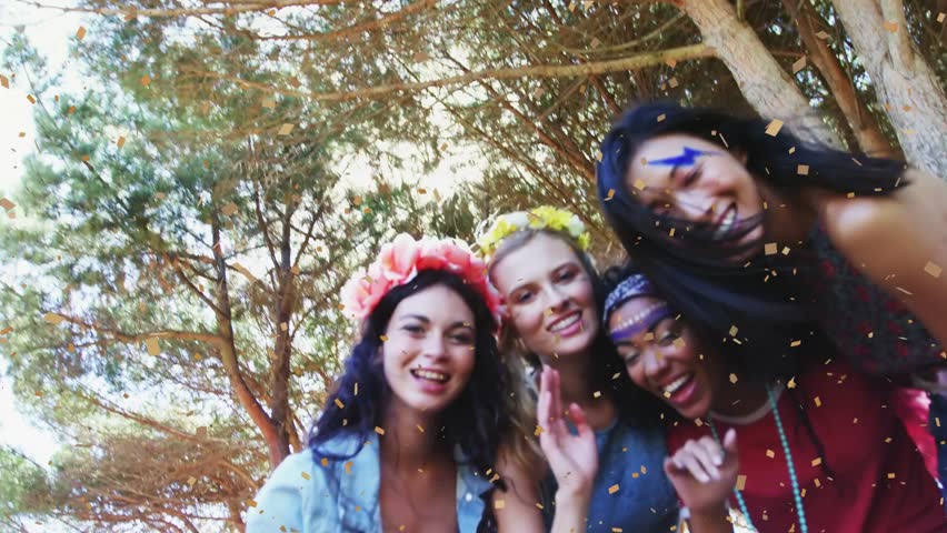 Camera starting four women leaning in greeting and waving for event confetti falling across faces. Outdoor, forest, pine, festival, celebration, friends, floral