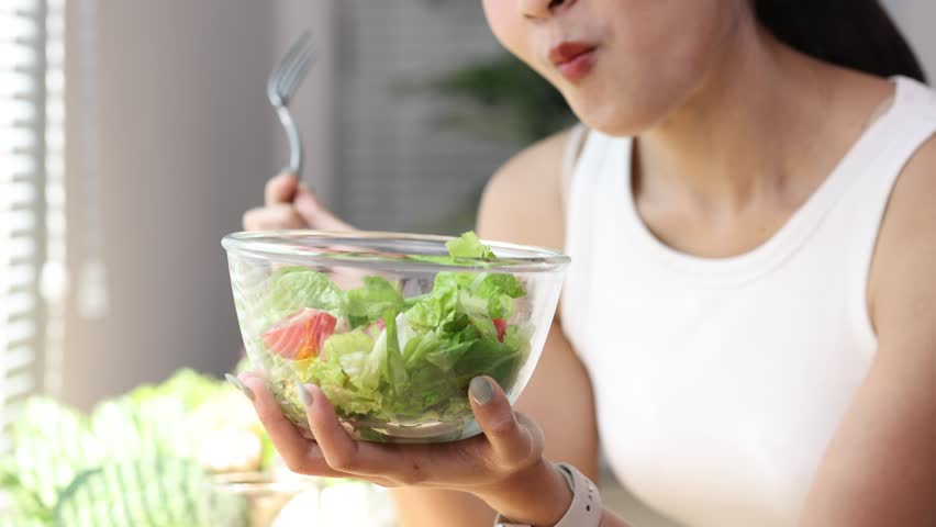 Young woman enjoying a healthy salad in a bright kitchen.