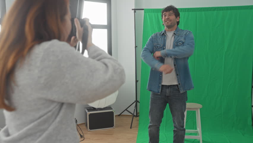 Man and woman photographers inspect dslr camera as woman gestures with hand and holds strap in studio; teaching collaboration.