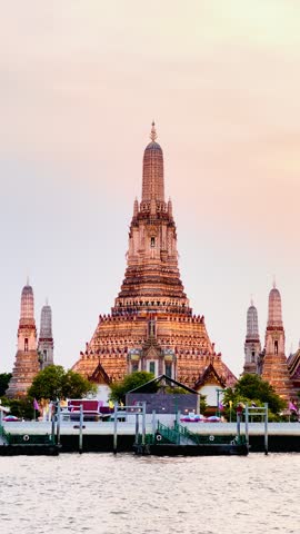 Wat Arun Ratchawararam in Bangkok, Thailand, with a bright golden orange sunset as the backdrop. The reflection of the temple on the water below creates a peaceful and elegant atmosphere.