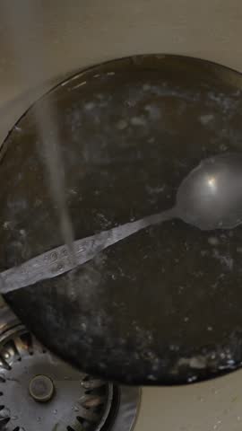 Water in motion running over metal spoon in dark bowl