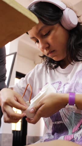 Portrait of a focused Colombian girl building a robotic arm while listening to music with wireless headphones inside an academic club in Neiva, Huila, Colombia. Concept of education, science and technology