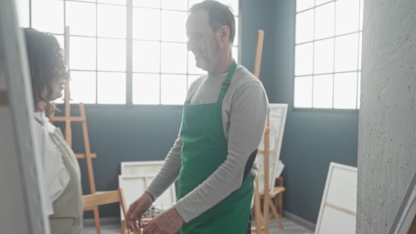 Man and woman painters embrace with arms around neck amid easels and canvases in studio; intimacy tenderness.