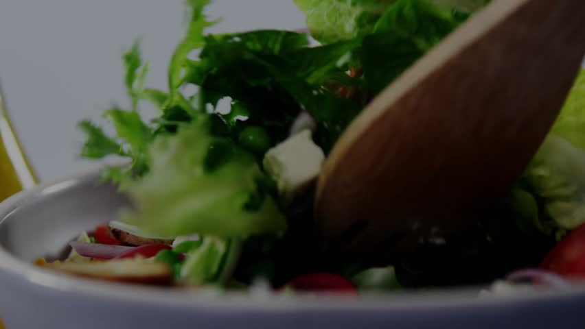 Hand holding wooden fork entering, tossing fresh salad in bowl, audio bars overlaying for food prep. Greens, tomatoes, onion, cheese, utensil, kitchen, toss