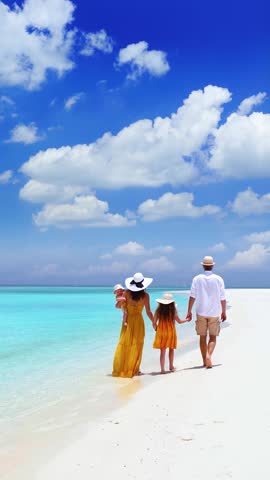 A elegant family in summer dresses walks on a tropical paradise beach with turquoise ocean and white sand during their vacation time