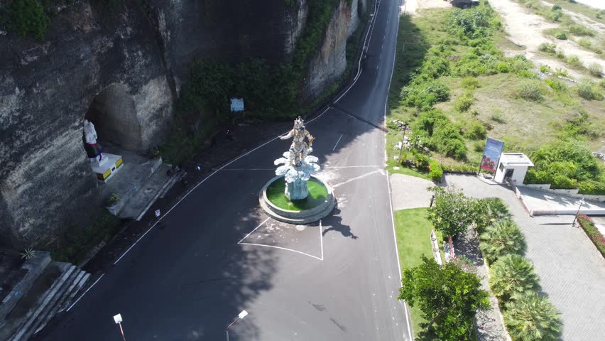 Cinematic aerial drone orbiting around iconic statue at Pandawa Beach entrance roundabout in Bali, Indonesia.