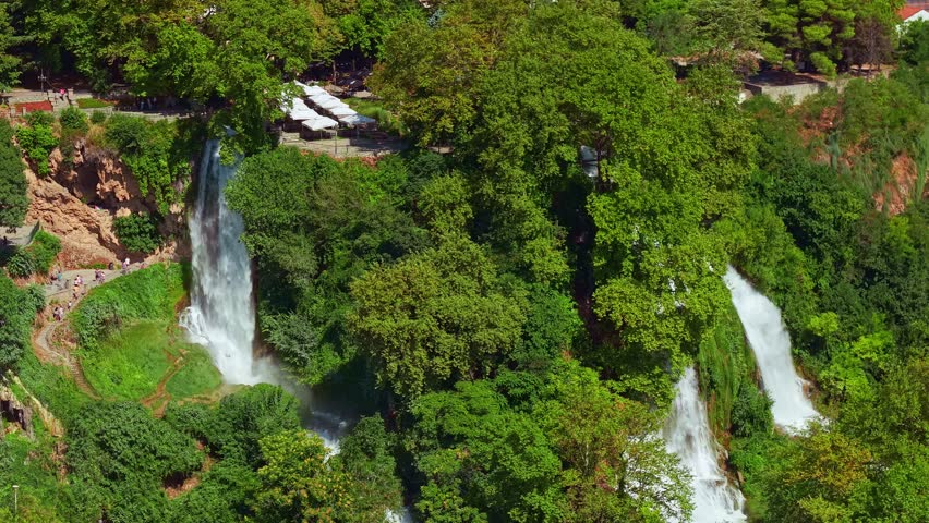 Aerial view of the powerful Edessa waterfalls cascading through dense green forest with the town in the distance, Greece