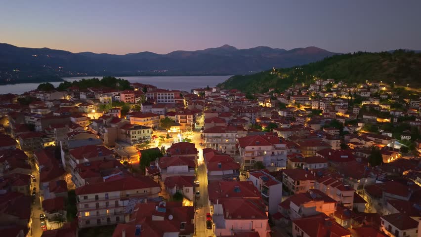 Beautiful night aerial view of Kastoria city lights reflecting in Lake Orestiada with mountains in the background at dusk, Greece