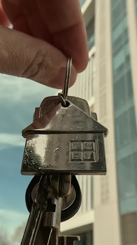 Vertical video. Moving to new apartment, buying or renting real estate. Hand holding keys in background of new building