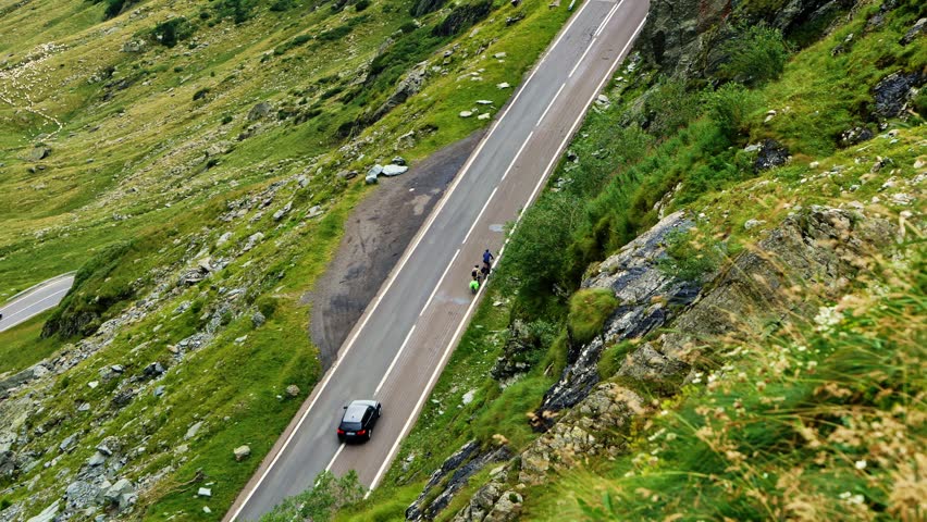 Handheld shot of cyclists riding on the steep Transfagarasan mountain road in Romania. Scenic view of car and bikers on asphalt serpentine winding through rocky alpine landscape