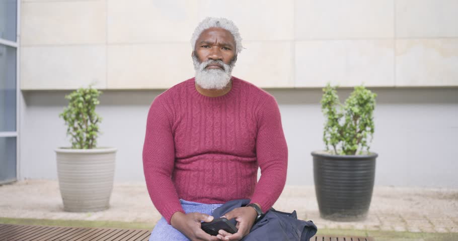 Senior African American man arriving at plaza bench with sunglasses, adjusting posture and laughing. Portrait, outdoor, casual, relaxed, urban, cheerful, lifestyle