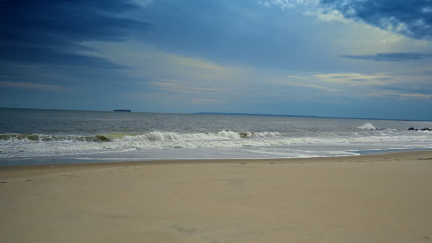 Sea gull flies low over the water on grey cloudy day. Raging waves roll to the shore.