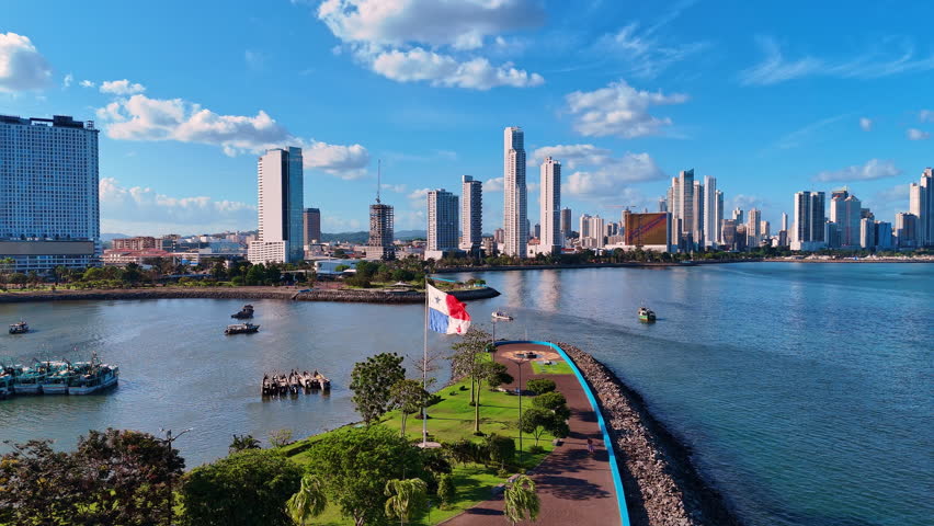 Panama flag on the pole flaps in the wind. Boat stand on the waterscape around the pier. Beautiful high-rise buildings in the backdrop.