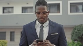Young man in navy suit and glasses covering mouth with hand while checking smartphone outside modern building; anxiety. - Powered by Shutterstock - Get 15% off with code: PIKWIZARD15