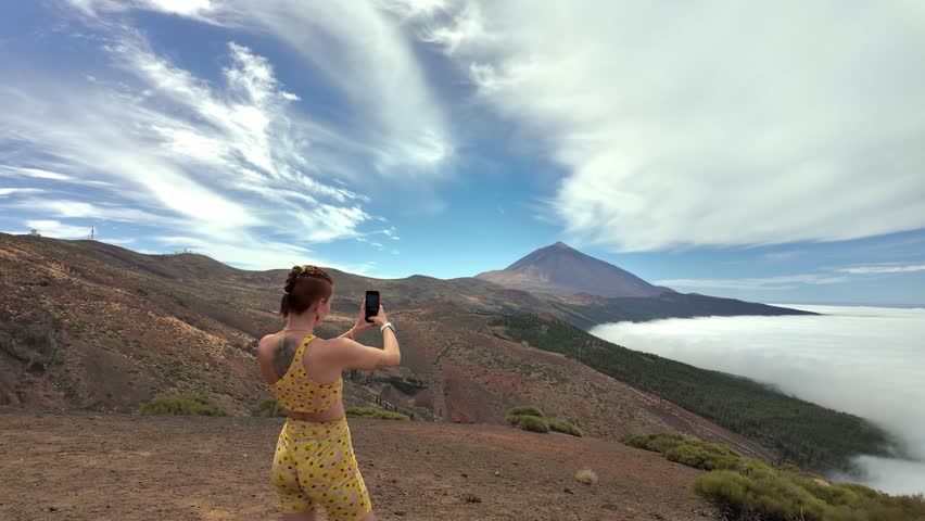 Female hiker taking a photo with her smartphone on a mountain. Beautiful landscape with the teide volcano and a sea of clouds below