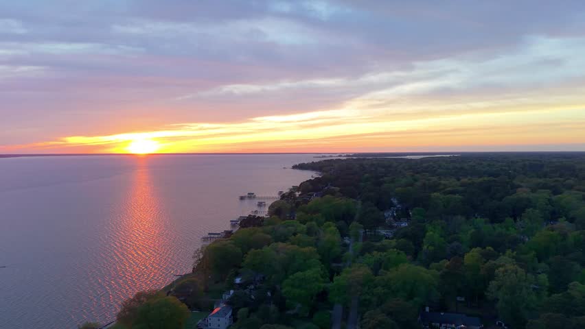 James River coastline in Newport News, Virginia, aerial sunset video, featuring luxury waterfront residential homes and a vibrant evening sky. 