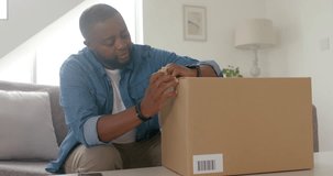 African American man inspecting tape, cutting with utility knife on box on sofa to retrieve order. Unboxing, package, livingroom, candid, lifestyle, delivery, opening - Powered by Shutterstock - Get 15% off with code: PIKWIZARD15