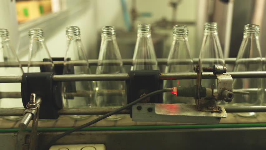 Close-up of industrial bottling equipment precisely filling glass containers with liquid during high-speed beverage production process in factory
