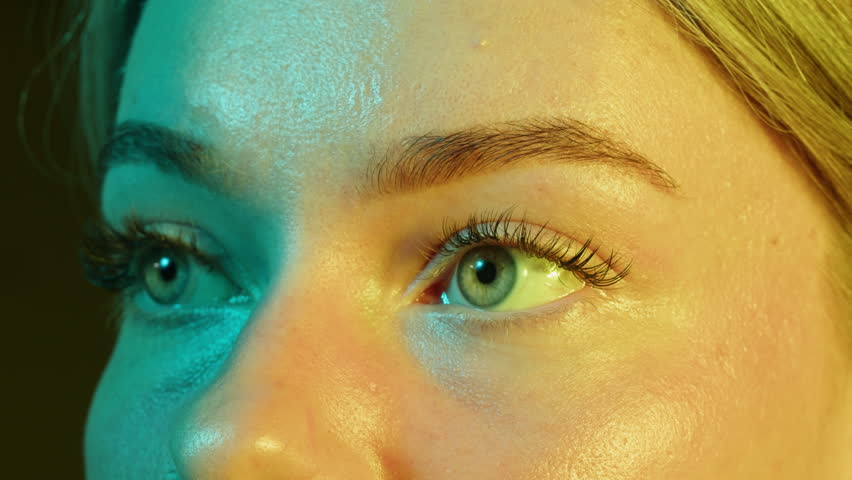 Close-up womans blinking eye with long eyelash and contact lens. Beauty make up of green eye with neon light.
