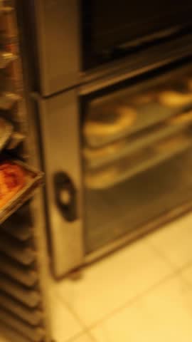 A professional baker taking a tray of freshly baked, hot mini pizzas out of a commercial oven and placing them on a display counter in a bakery.
