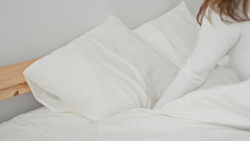 Woman sleeping and turning in bed, hand on stomach and holding a pillow against her head in a bedroom building; serenity comfort rest.