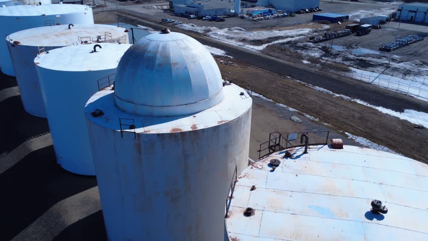 Drone flying over a dome-shaped structure atop large white petrochemical tanks connected by multiple pipelines in an industrial storage facility.
