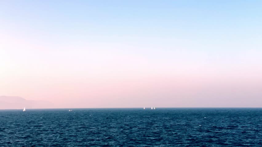 Yachts sailing on calm blue ocean waters under clear sunny skies