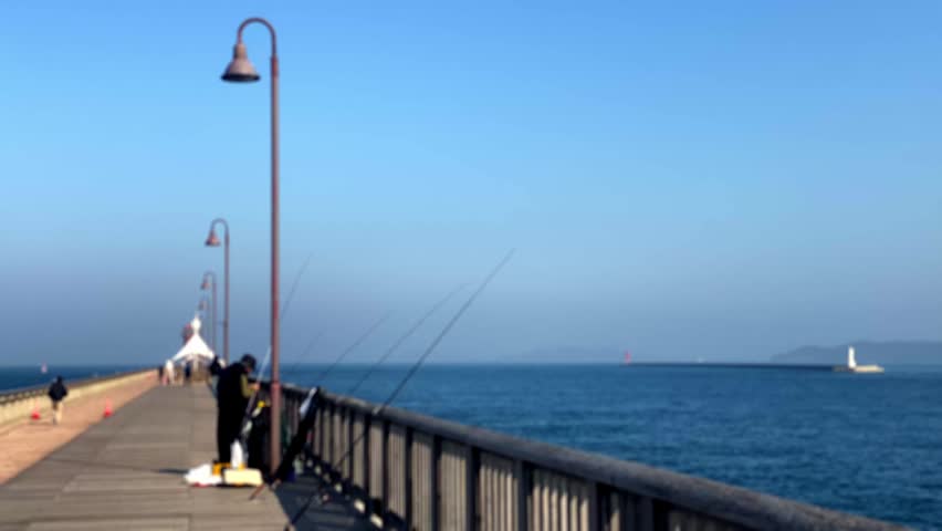 People fishing on ocean pier with others walking by on calm blue water