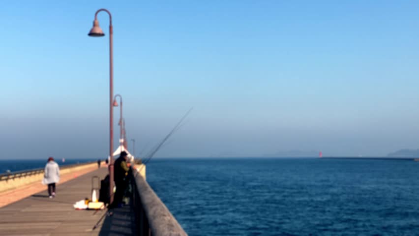 People fishing on ocean pier with others walking by on calm blue water
