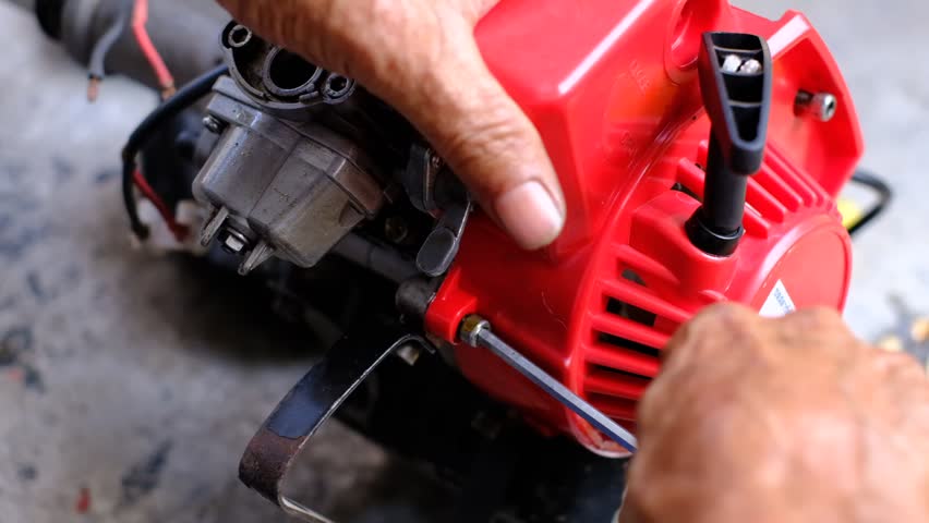 A man is working on a red engine. He is using a screwdriver to remove a bolt