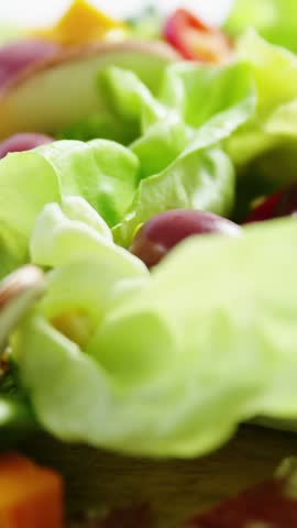 Vertical video: Camera pulling back and focusing is revealing green salad on wood board for styling. Lettuce, cucumber, olives, mushrooms, corn, pepper, vertical video