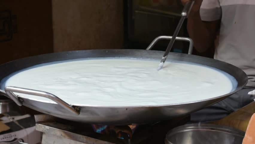 Fresh cow milk boiling in a large metal pot at a roadside sweet shop in Varanasi, India. Traditional preparation scene with steam, heat, and authentic street food culture.