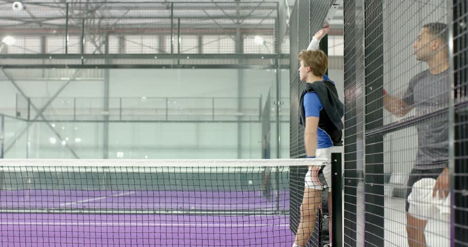 White male in blue gear tracking incoming ball, crouching and celebrating win on purple padel court. Athletic, teamwork, sport, recreation, energetic, victory, active