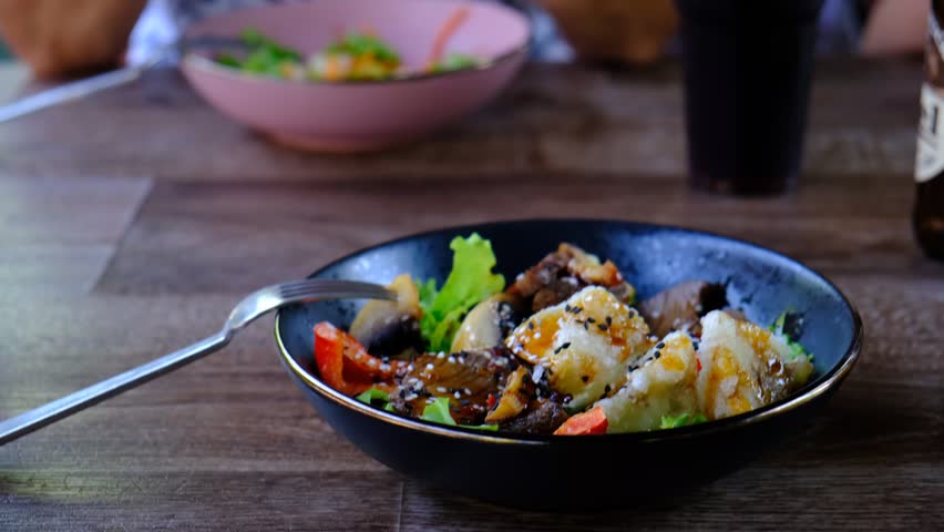 Stir-fried vegetables with teriyaki sauce. Spicy Asian dish with sliced meat fillet, hot pepper, bell pepper, carrots and black white sesame seeds, black plate bowl
